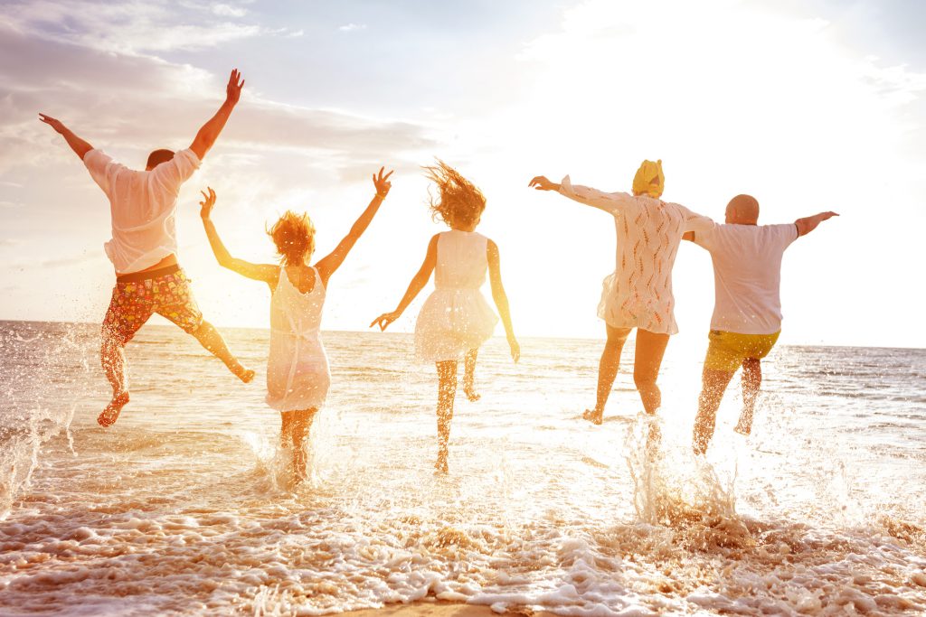 Group of five happy peoples run and jump to sea beach against sunset sun